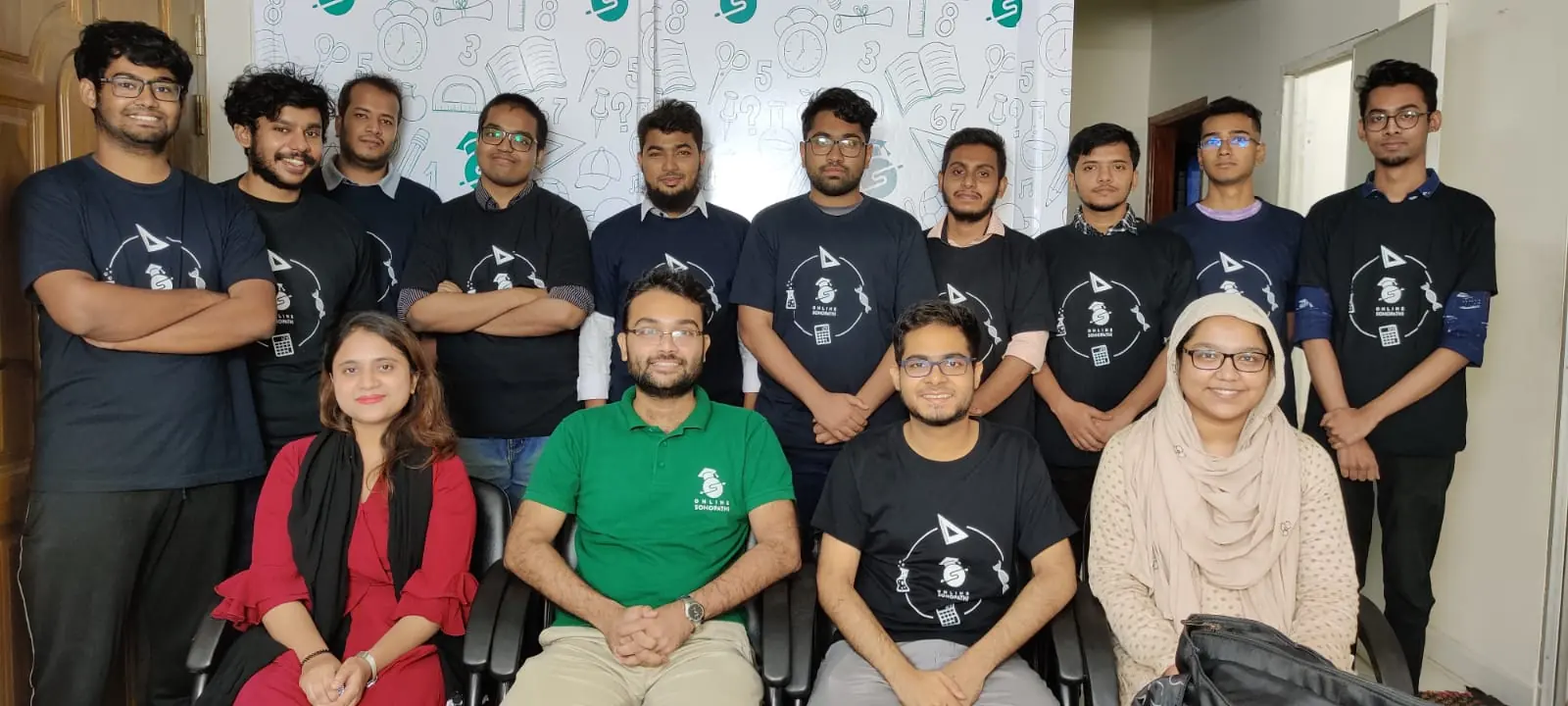 The Sohopathi team in 2021, most of them in Sohopathi t-shirts, posing in front of a wall of doodles.